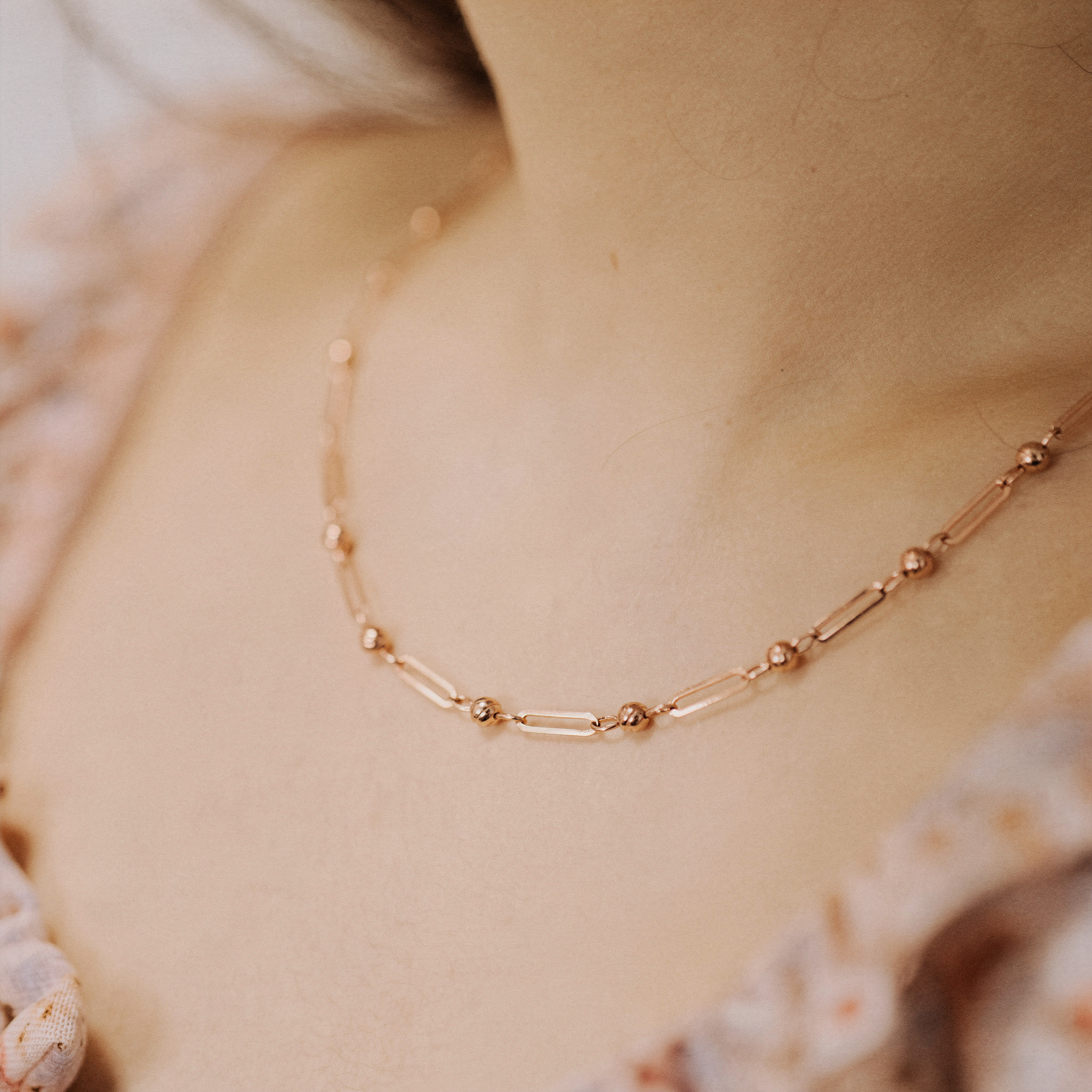 {
  "scene": "A close-up lifestyle shot of a person's neck and collarbone area, exactly matching the composition, skin tone, and floral clothing from image 1, but featuring the rose gold necklace from