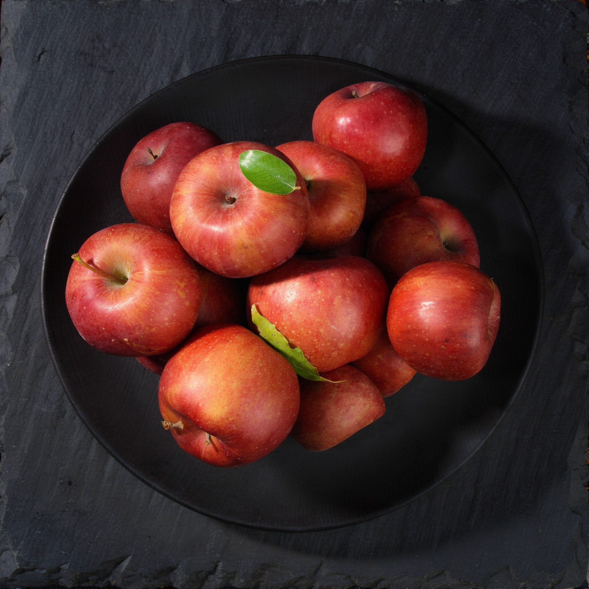 {
  "scene": "A professional culinary flat lay photography scene where the food items from image 2 are arranged onto the plate in image 1. The background is a dark, textured black slate surface with o