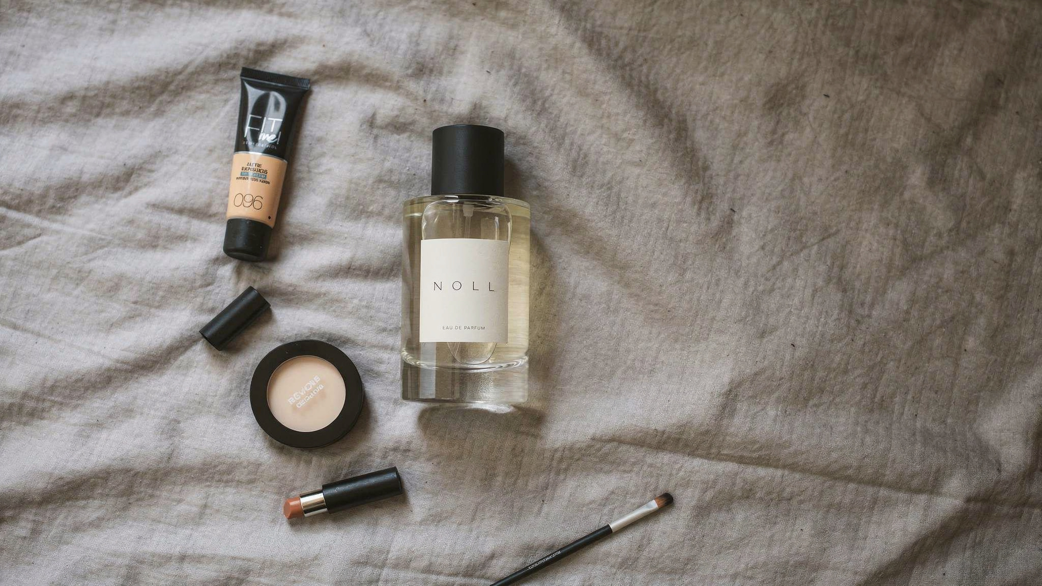 {
  "scene": "A top-down flat lay photography scene set on a rumpled, textured light gray linen fabric, exactly as shown in image 1. The scene maintains the same arrangement of props from image 1, inc