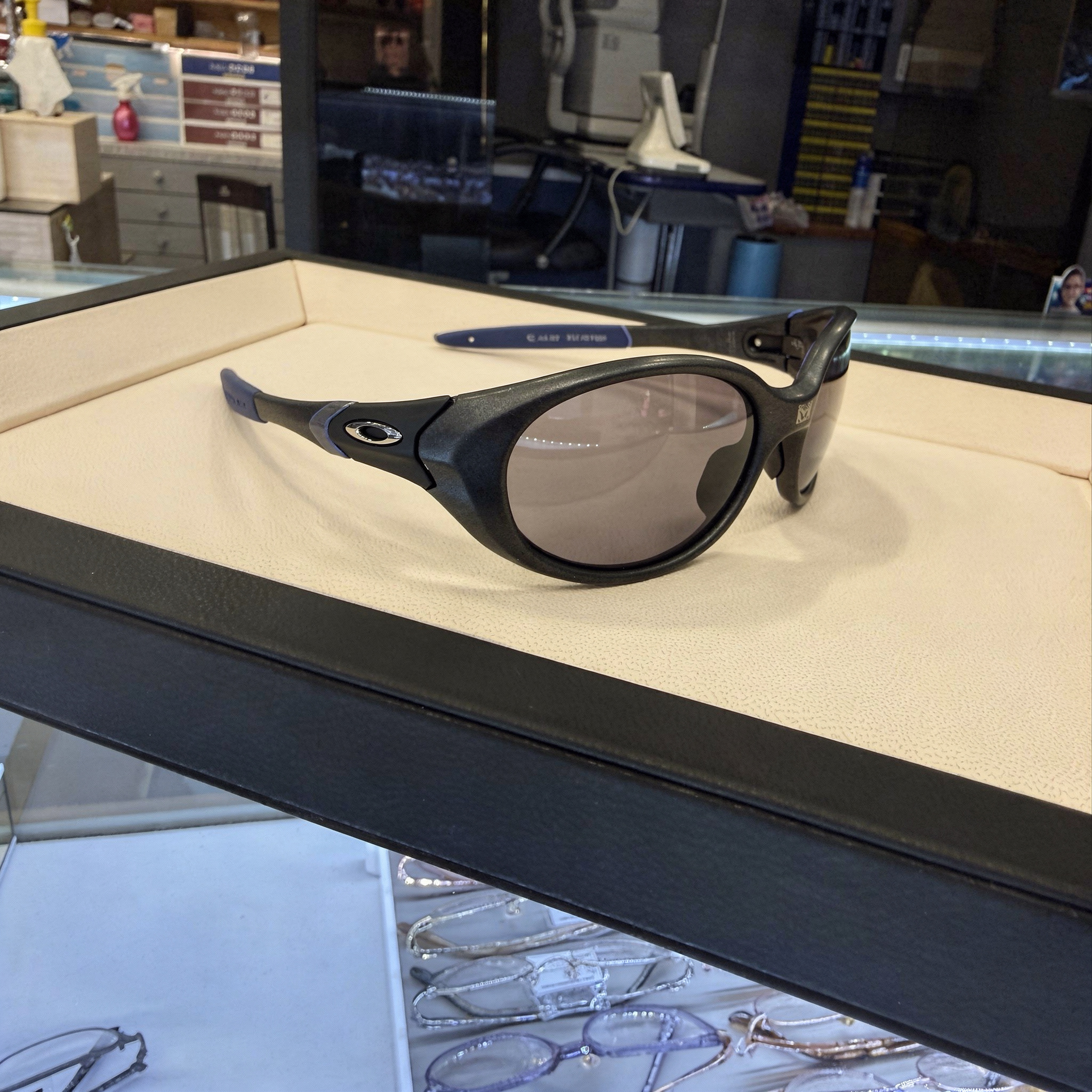 {
  "scene": "A professional product replacement shot where the sunglasses in image 1 are replaced by the specific product from image 2. The setting is a brightly lit eyewear boutique. The product fro