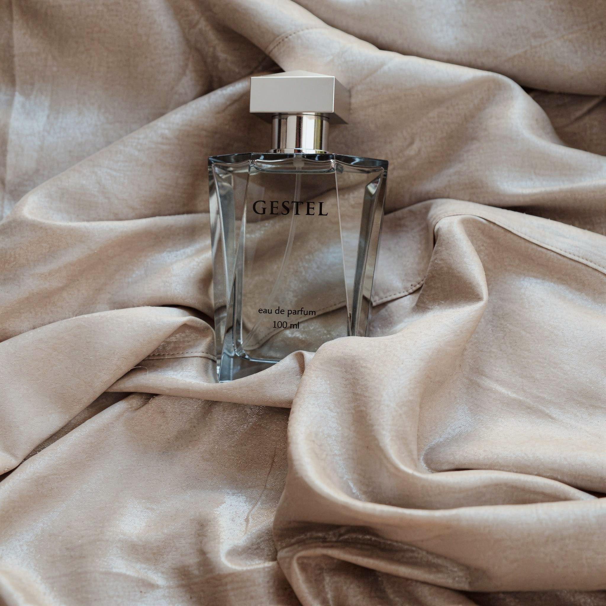 {
  "scene": "A high-end product photography shot using the exact draped fabric background from image 1, but replacing the original item with the perfume bottle from image 2. The background consists o