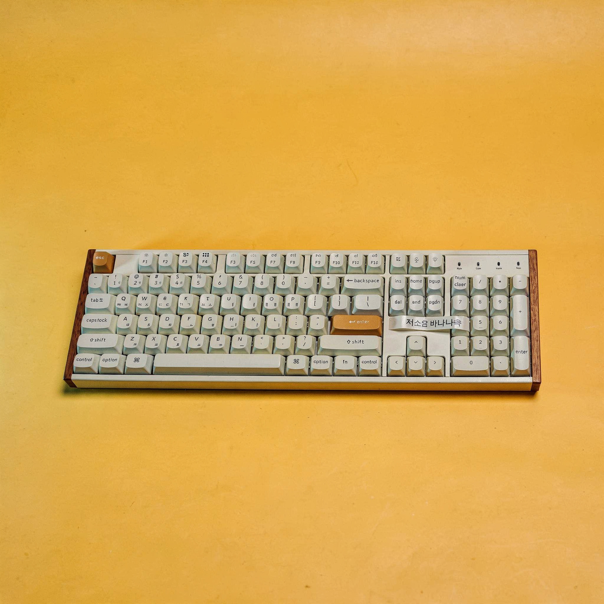 {
  "scene": "A professional studio product shot replacing the small toy in image 1 with the full-sized mechanical keyboard from image 2. The keyboard is centered on the same seamless vibrant yellow-o