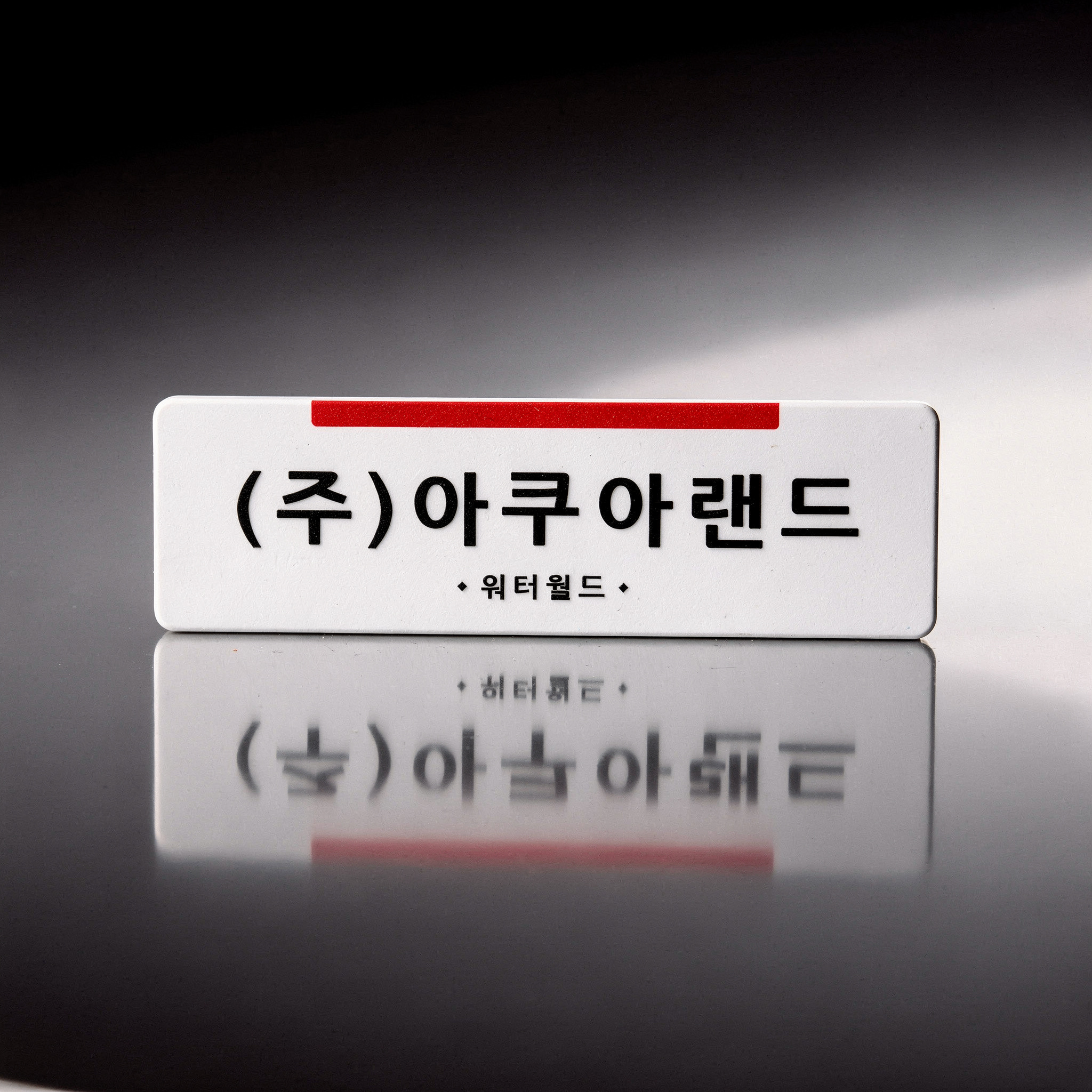 {
  "scene": "A product replacement edit where the cosmetic jar in image 1 is replaced by the corporate signage from image 2. The new subject is positioned on the same highly reflective, polished dark