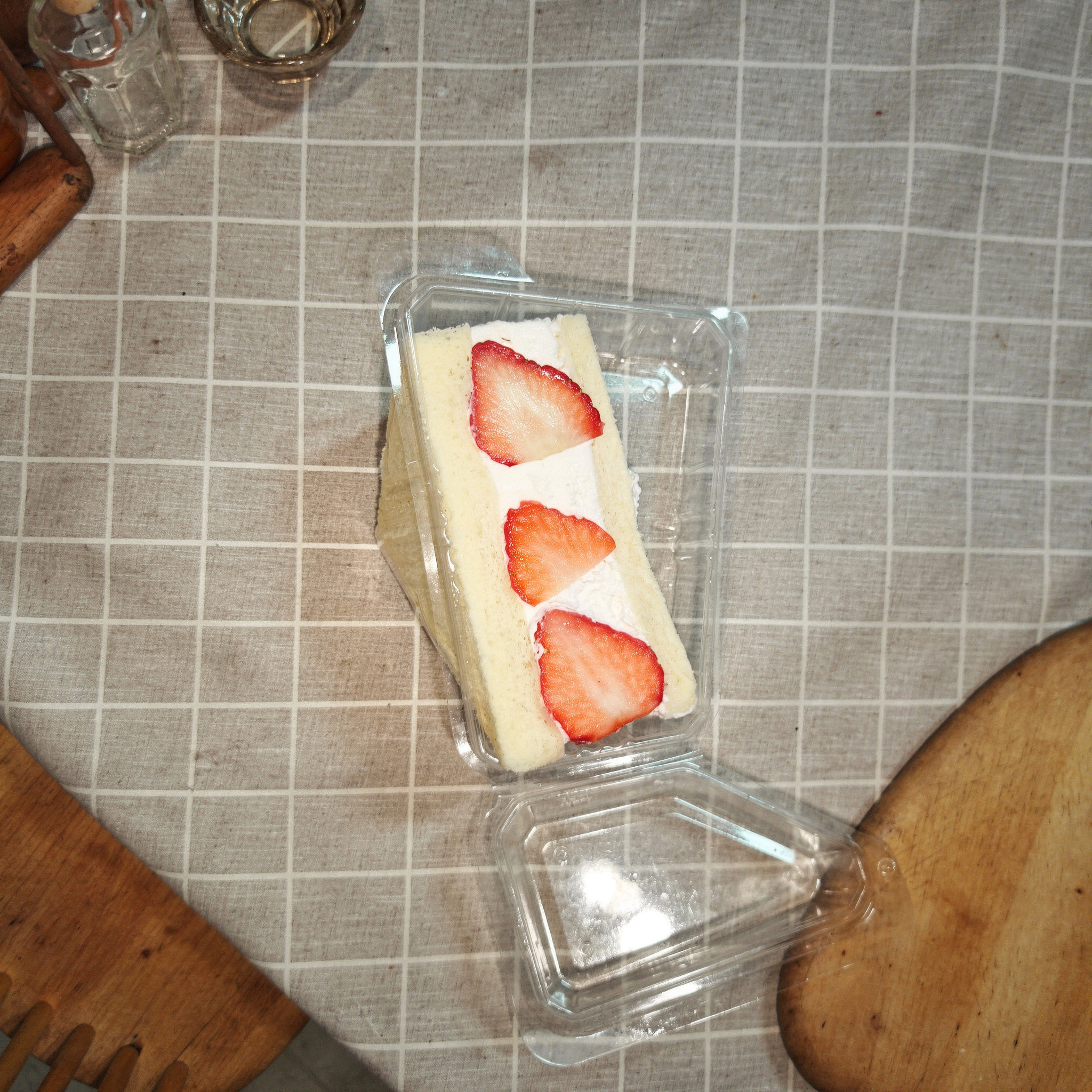 {
  "scene": "A top-down view of a cozy dining table setting from image 1. The surface is covered with a grey and white grid patterned tablecloth. Subtle glimpses of a wooden floor, a wooden cutting b